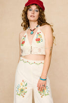 Woman wearing a red cap, floral embroidered top, and colourful necklace against a beige background - front view