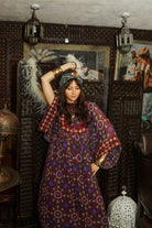 Model dancing wearing a 70s style bohemian maxi dress in a printed purple fabric with hand embroidery