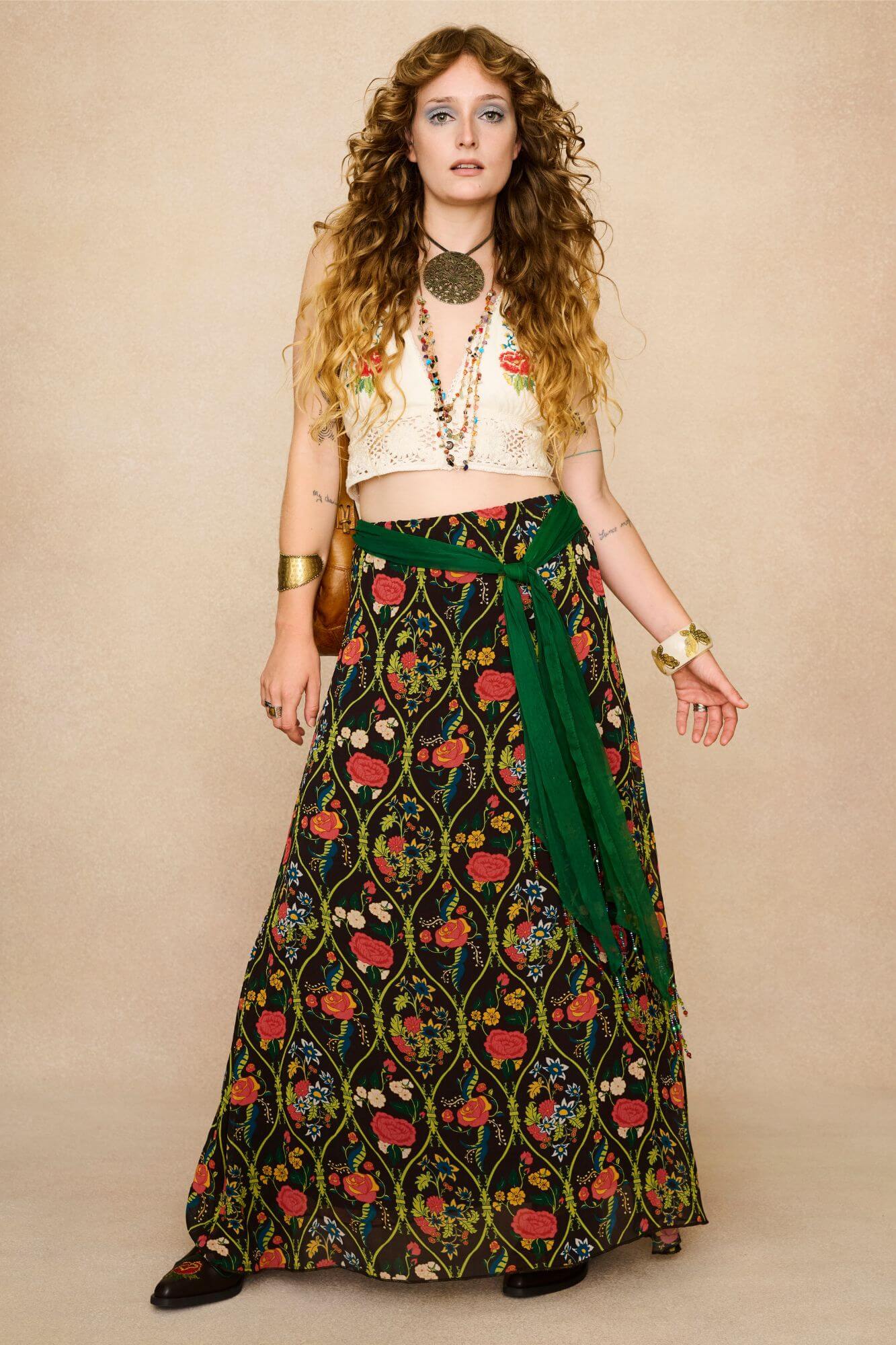 Model wearing a long 70s style floral skirt and white top with a beige background - front view