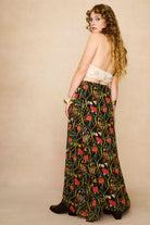 Model wearing a long 70s style floral skirt and white top with a beige background - back view