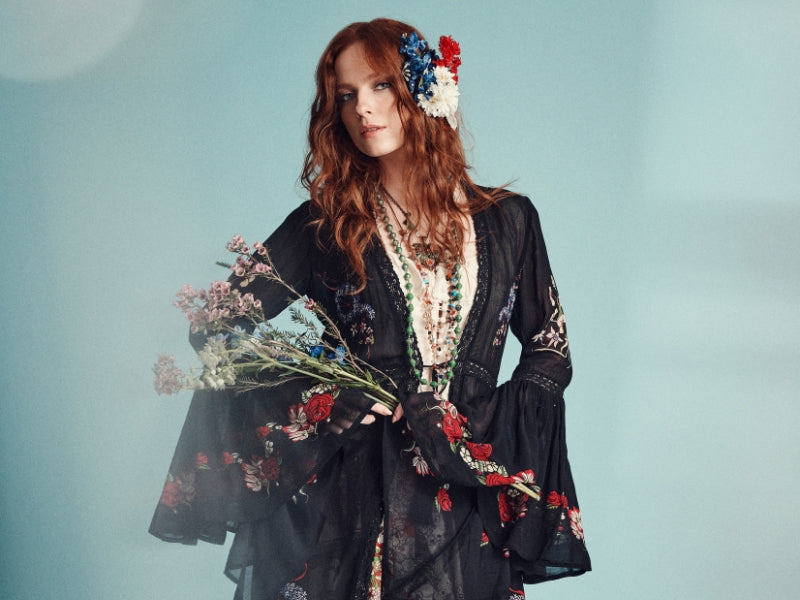 Woman in a black embroidered 70s duster holding flowers
