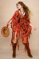 Model wearing a vibrant red and black patterned dress cape with fringe against a beige background - Front view