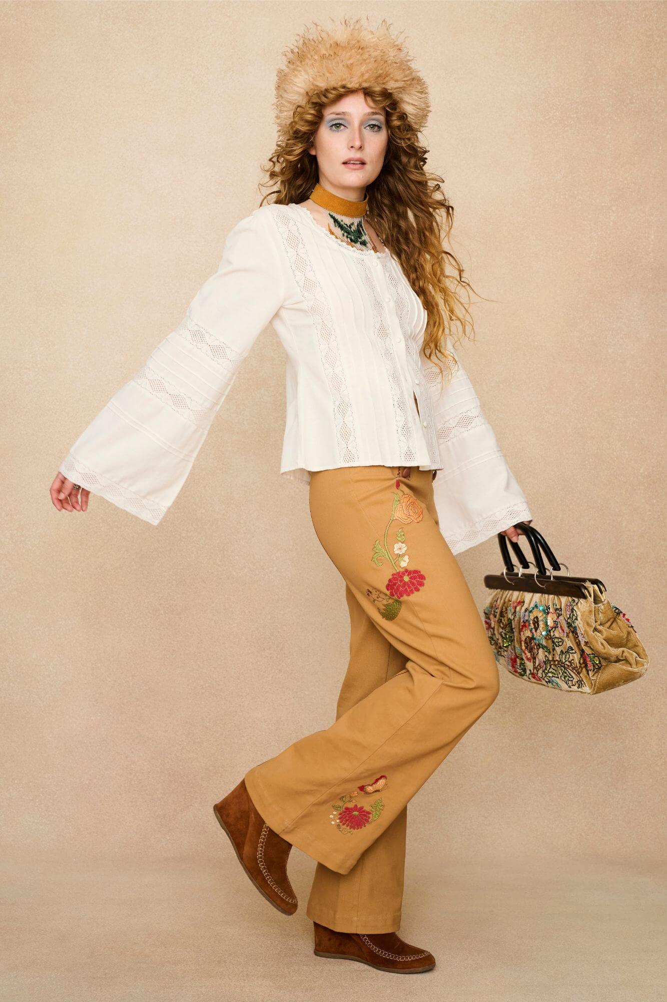 Woman wearing a white lace blouse and 70s style pants against a beige background - side movement view