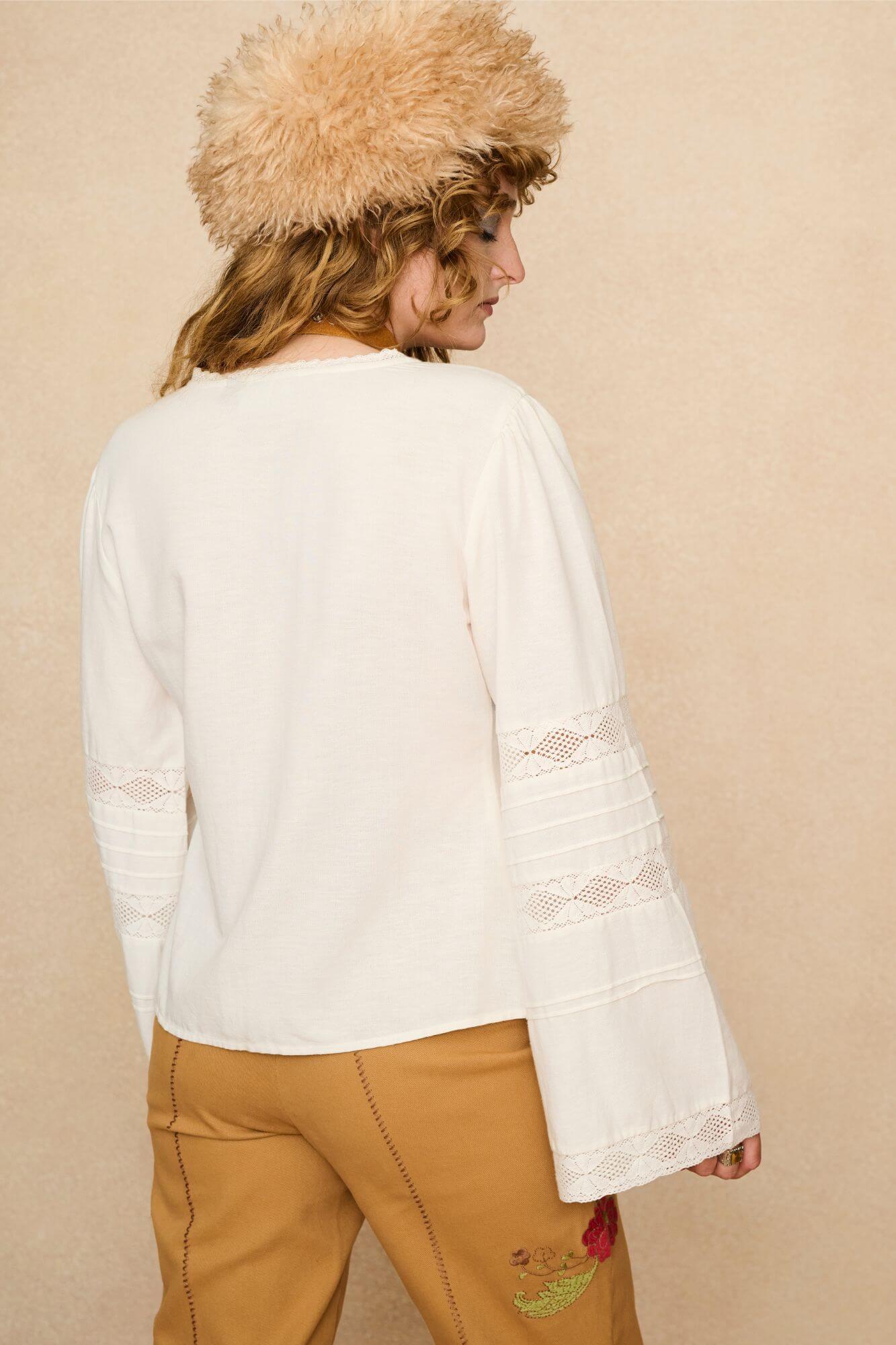 Woman wearing a white lace blouse and 70s style pants against a beige background - back view