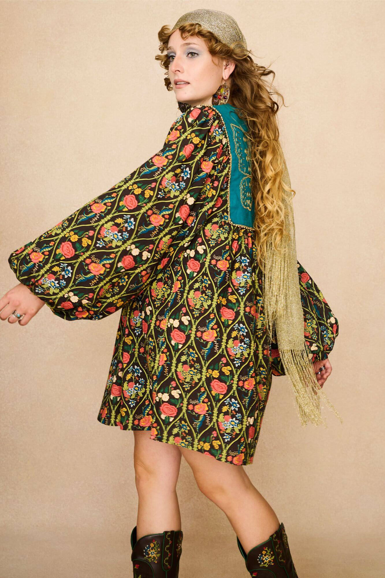 Model wearing a 70s style floral mini dress and matching boots against a beige background - movement