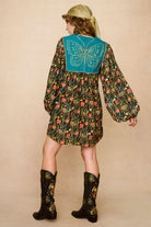 Model wearing a 70s style floral mini dress and matching boots against a beige background - back view