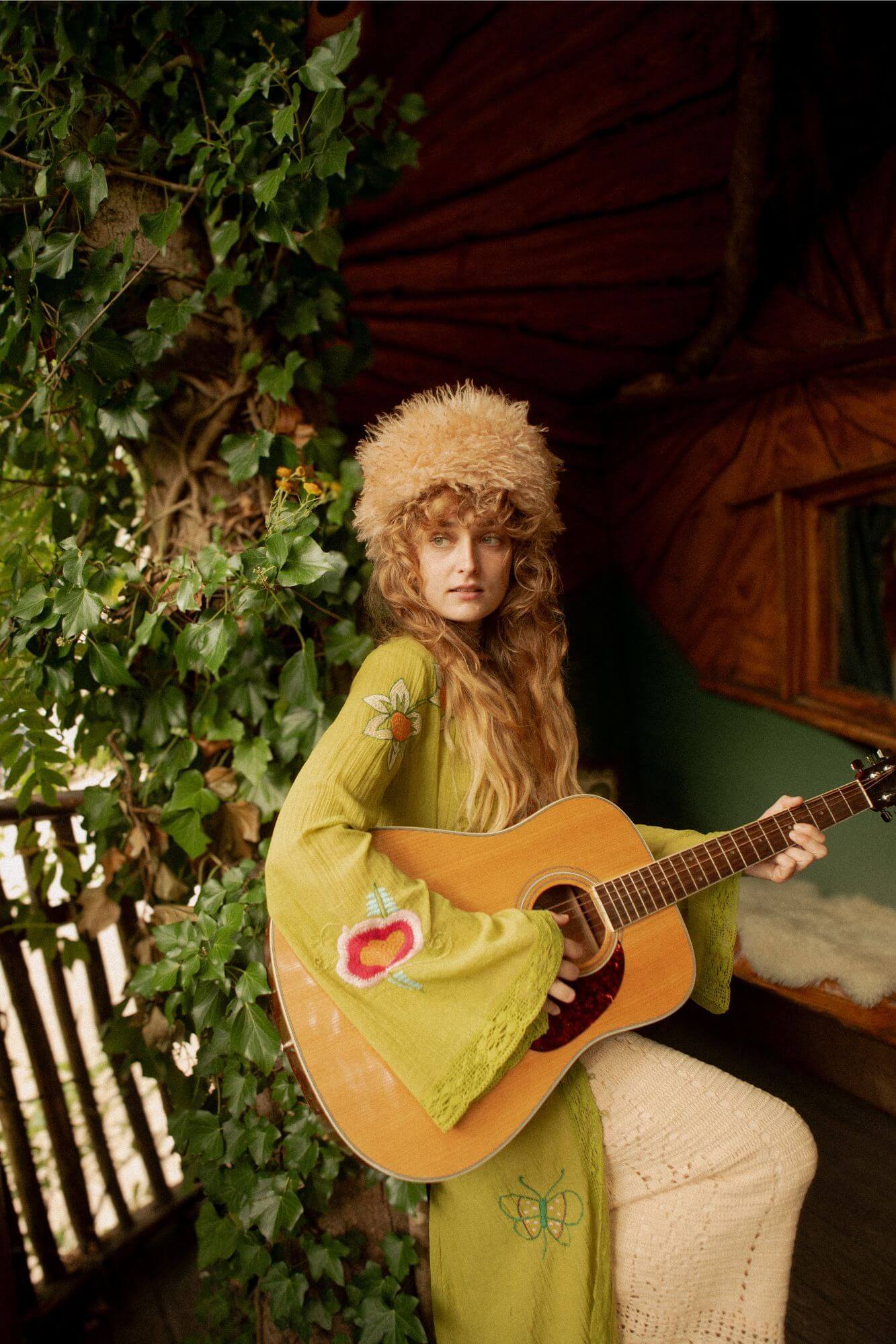 Woman in a green dress and hat playing an acoustic guitar outdoors.
