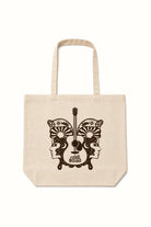 A natural canvas tote bag with a dark brown graphic print of a guitar and butterfly wings featuring stylized faces and sunburst patterns, shown against a plain white background.