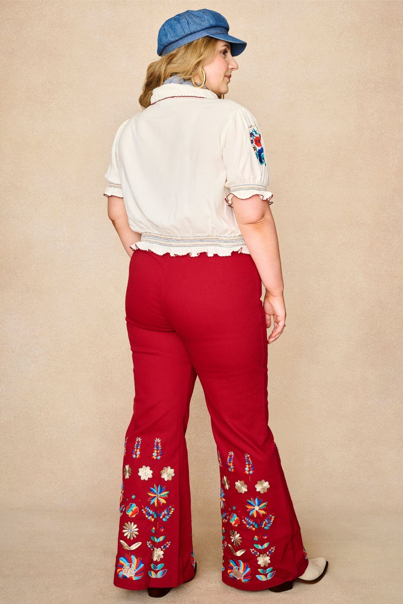 Model wears red flared trousers by The Hippie Shake, crafted from soft cotton twill with a gentle stretch, adorned with glowing floral vines and golden lurex - back view