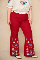Model wears red flared trousers by The Hippie Shake, crafted from soft cotton twill with a gentle stretch, adorned with glowing floral vines and golden lurex - close up view