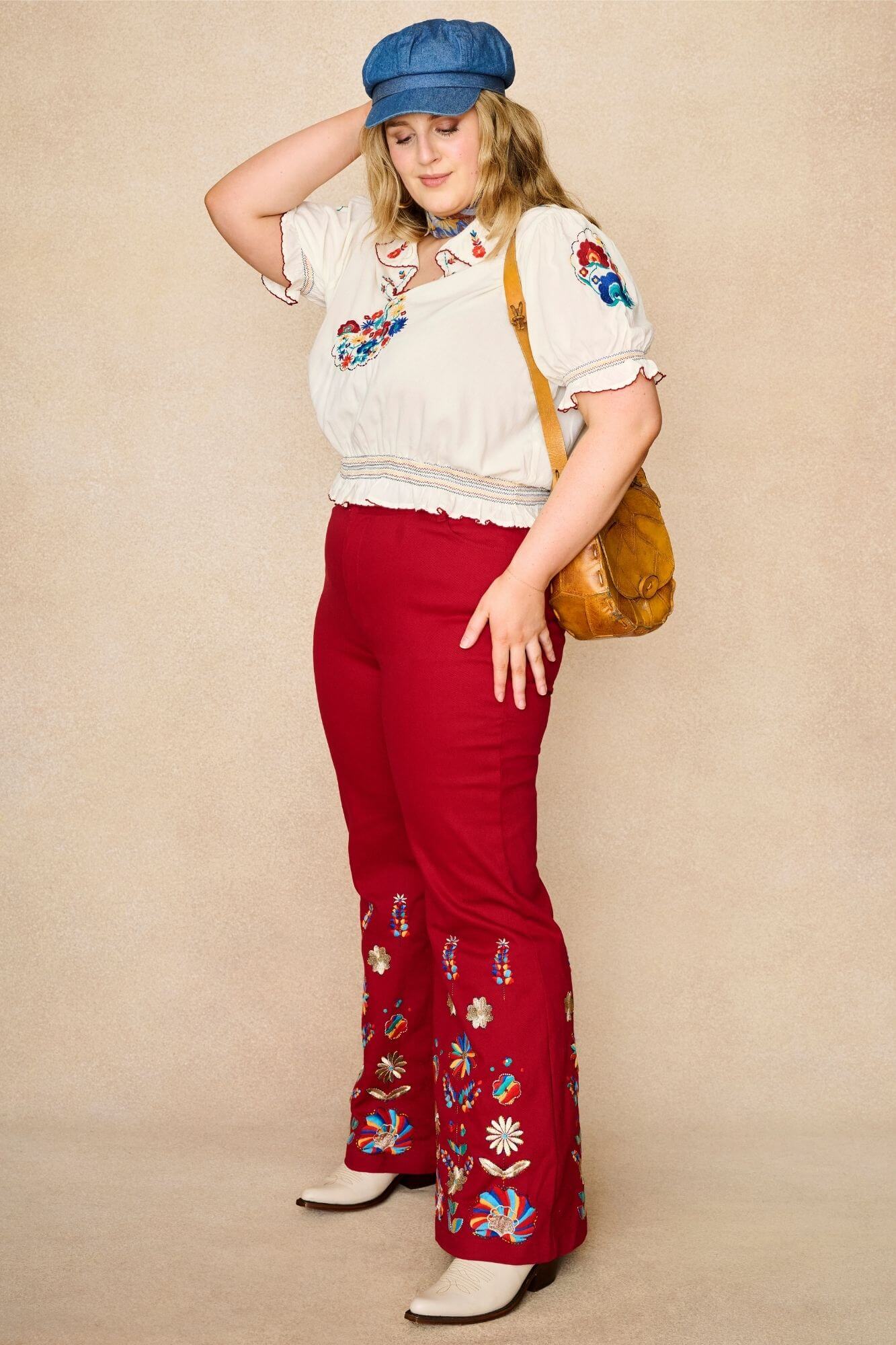 Model wears red flared trousers by The Hippie Shake, crafted from soft cotton twill with a gentle stretch, adorned with glowing floral vines and golden lurex - standing side view