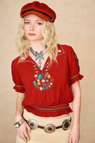 Model wears red floral embroidered Penny Lane blouse in soft cotton with shirred details. A vintage-inspired boho blouse made for everyday and festival styling by The Hippie Shake. Close up front view