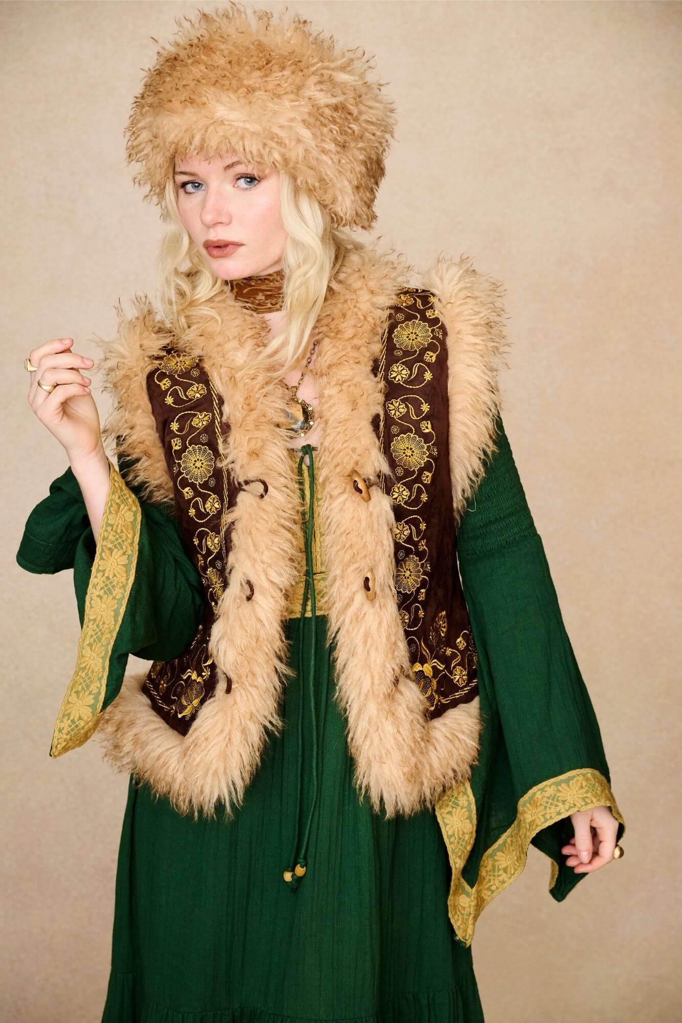 Model wears brown embroidered Penny Lane vest in faux suede with faux fur trim. A 70s-inspired boho layering piece made for vintage and festival styling by The Hippie Shake - front view paired with green dress