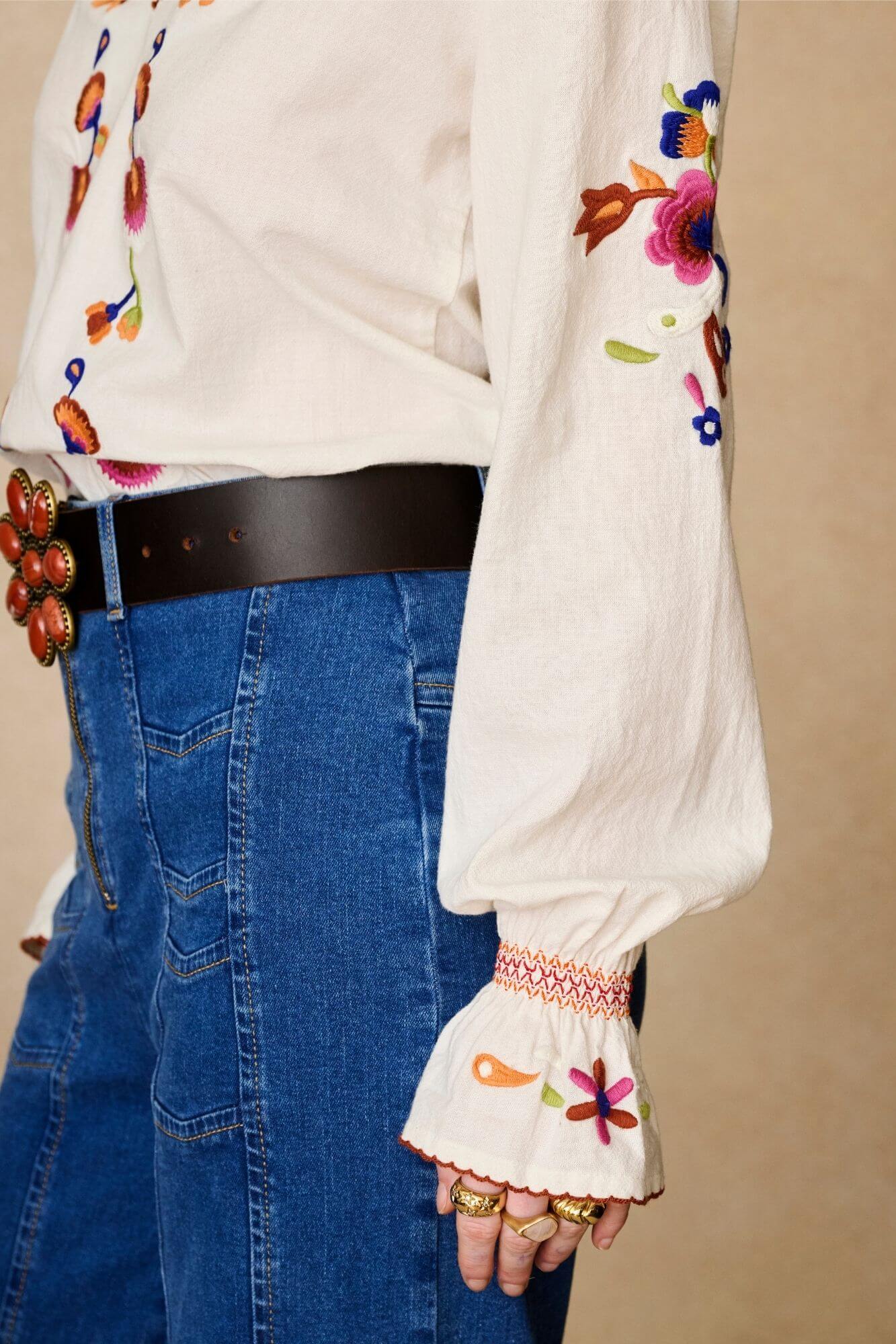 Model wears cream embroidered blouse in textured cotton with floral detailing and balloon sleeves. A 70s-inspired boho blouse made for everyday vintage styling by The Hippie Shake - sleeves detail