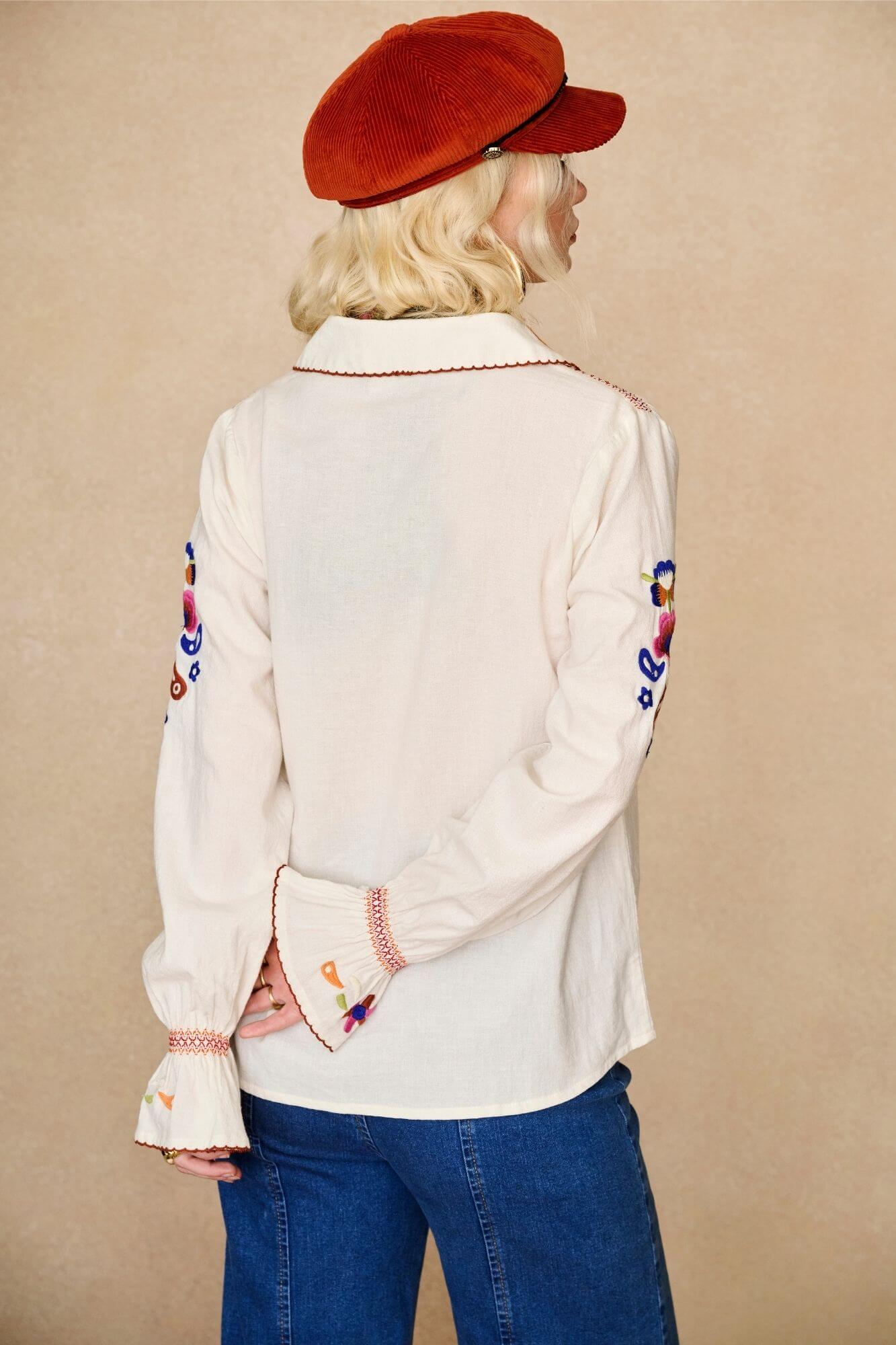 Model wears cream embroidered blouse in textured cotton with floral detailing and balloon sleeves paired with flared denim jeans. A 70s-inspired boho blouse made for everyday vintage styling by The Hippie Shake - back view