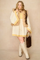 Model wears brown embroidered Penny Lane vest in faux suede with faux fur trim. A 70s-inspired boho layering piece made for vintage and festival styling by The Hippie Shake - front view paired with cream dress