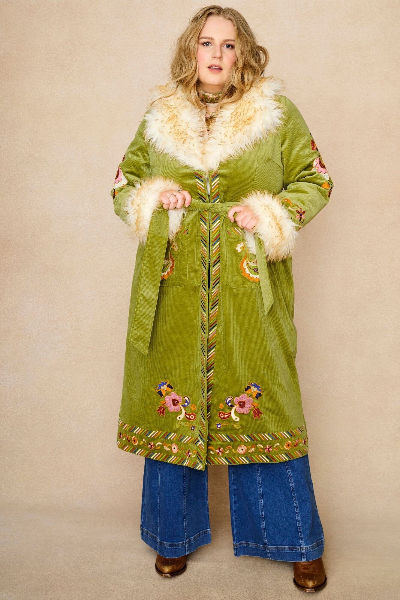 Model wears green embroidered Penny Lane coat in cotton corduroy with faux fur trim. A 70s-inspired statement coat made for bohemian, vintage styling by The Hippie Shake - wrapped front view