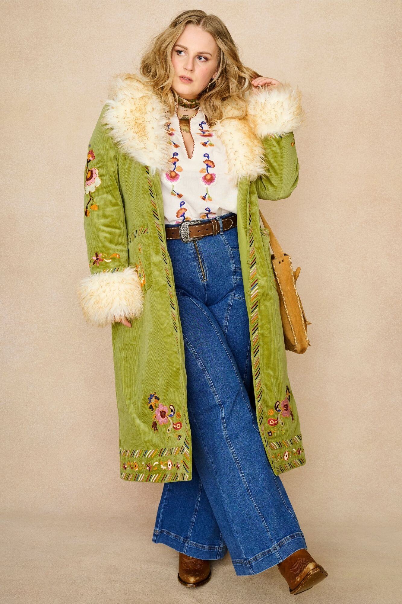 Model wears green embroidered Penny Lane coat in cotton corduroy with faux fur trim. A 70s-inspired statement coat made for bohemian, vintage styling by The Hippie Shake - leg out front view