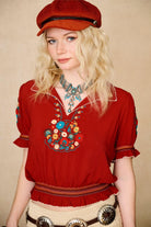 Model wears red floral embroidered Penny Lane blouse in soft cotton with shirred details. A vintage-inspired boho blouse made for everyday and festival styling by The Hippie Shake. Front view