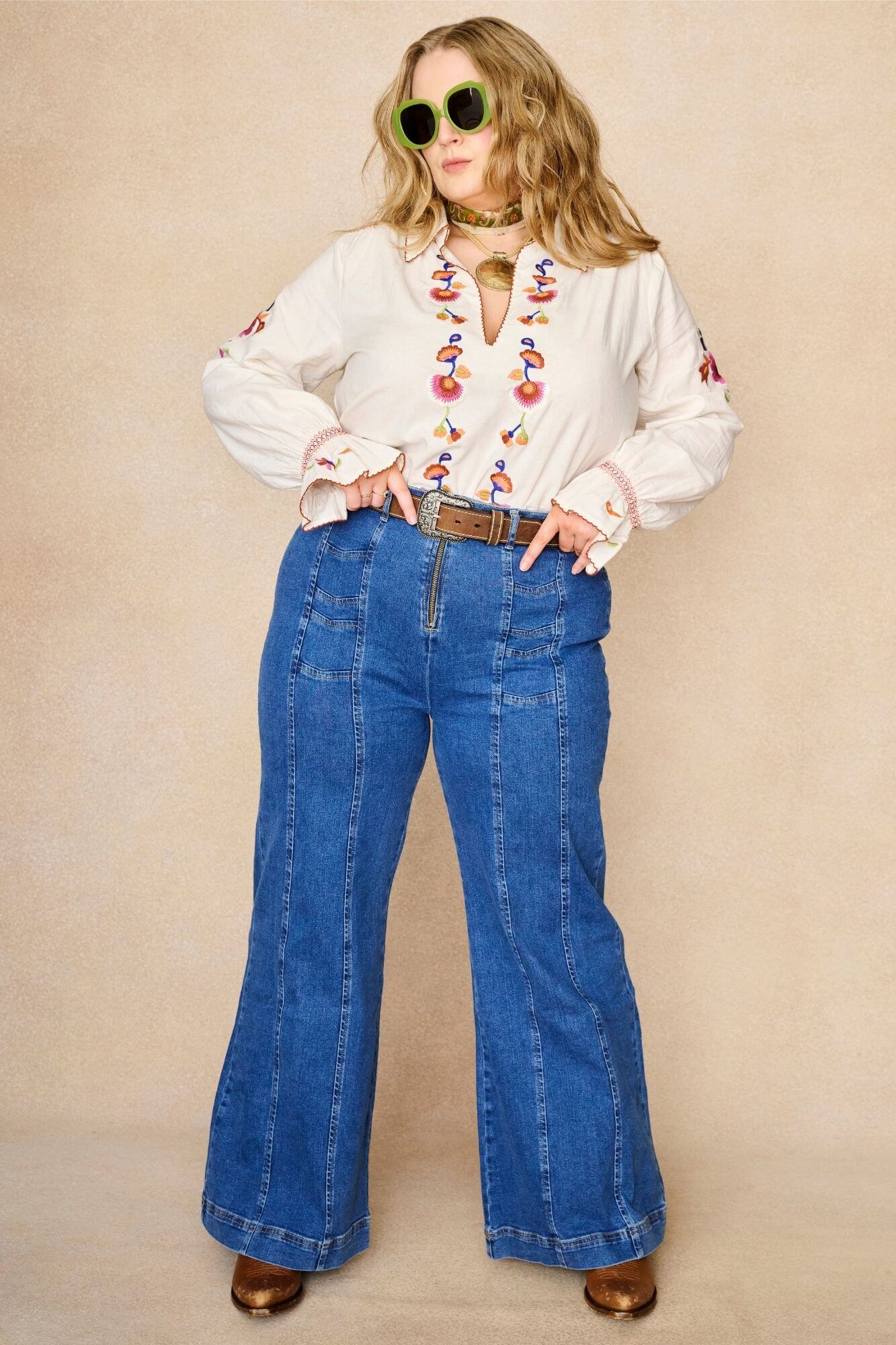 Model wears cream embroidered blouse in textured cotton with floral detailing and balloon sleeves paired with flared denim jeans. A 70s-inspired boho blouse made for everyday vintage styling by The Hippie Shake - standing front view
