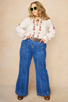 Model wears cream embroidered blouse in textured cotton with floral detailing and balloon sleeves paired with flared denim jeans. A 70s-inspired boho blouse made for everyday vintage styling by The Hippie Shake - standing front view