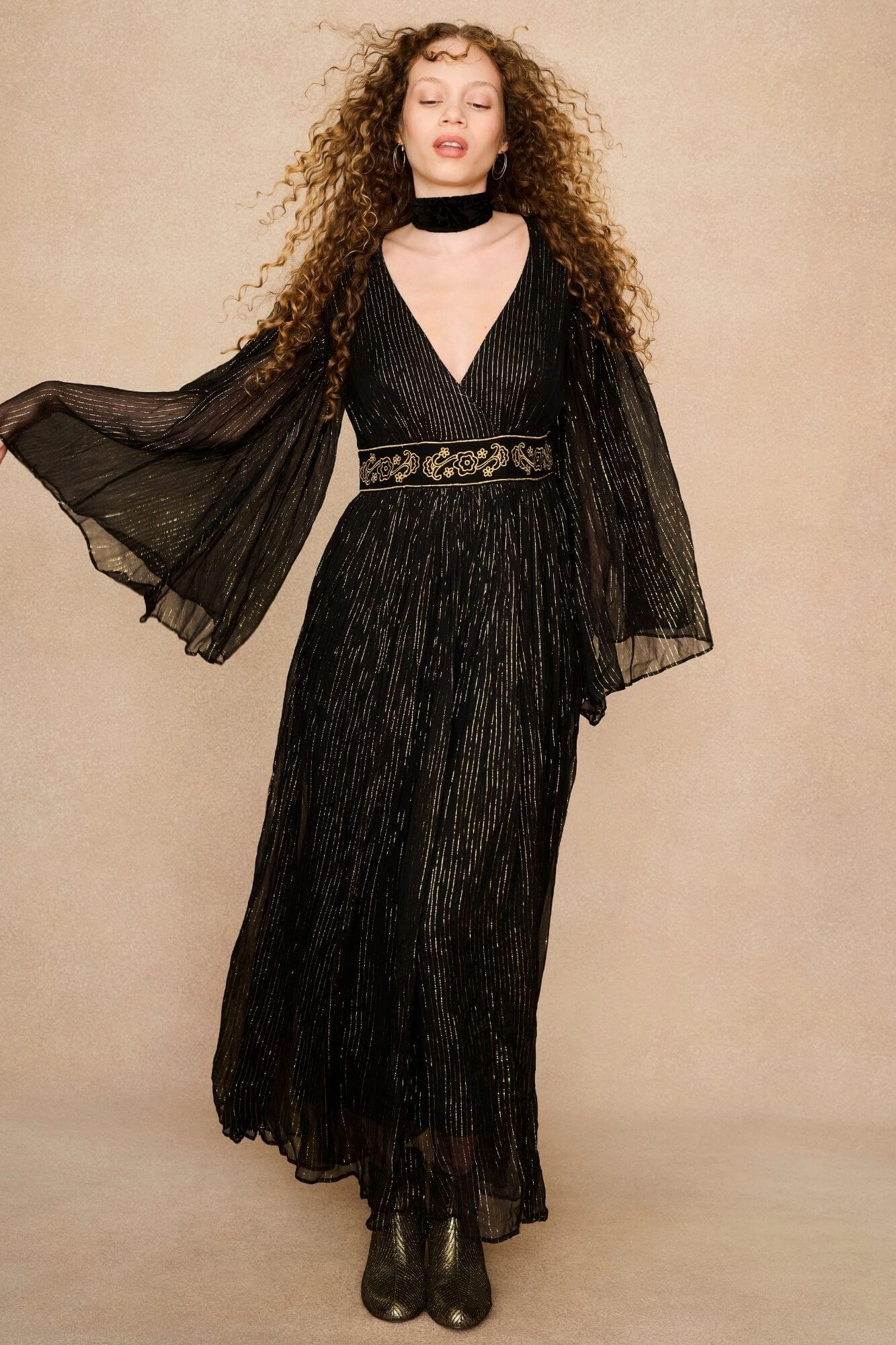 A model wearing a black maxi dress with sheer long flowy sleeves by the Hippie Shake