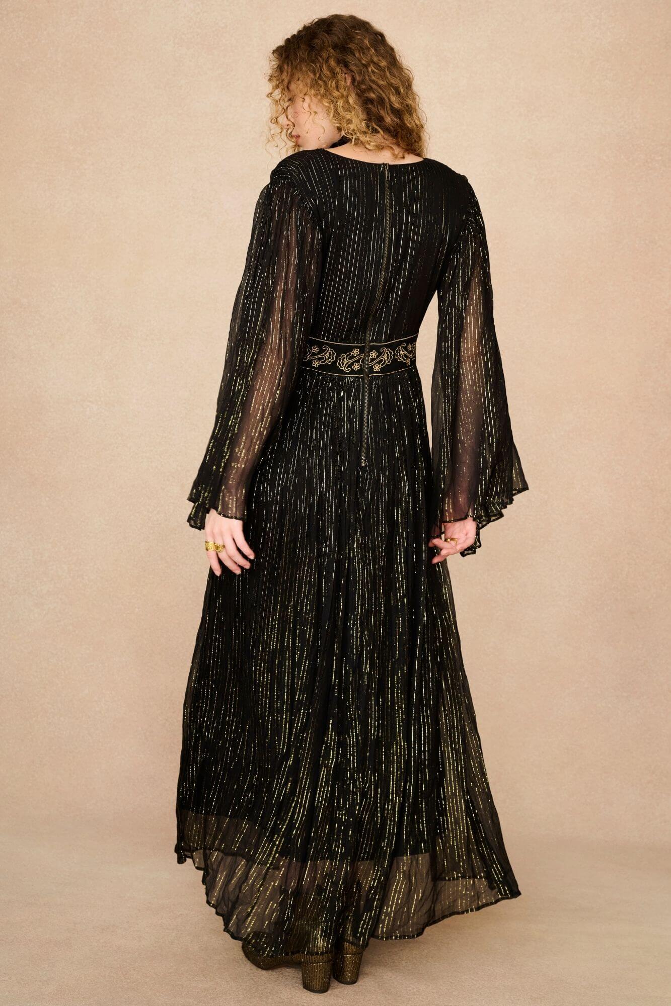A model wearing a black maxi dress with sheer long flowy sleeves by the Hippie Shake