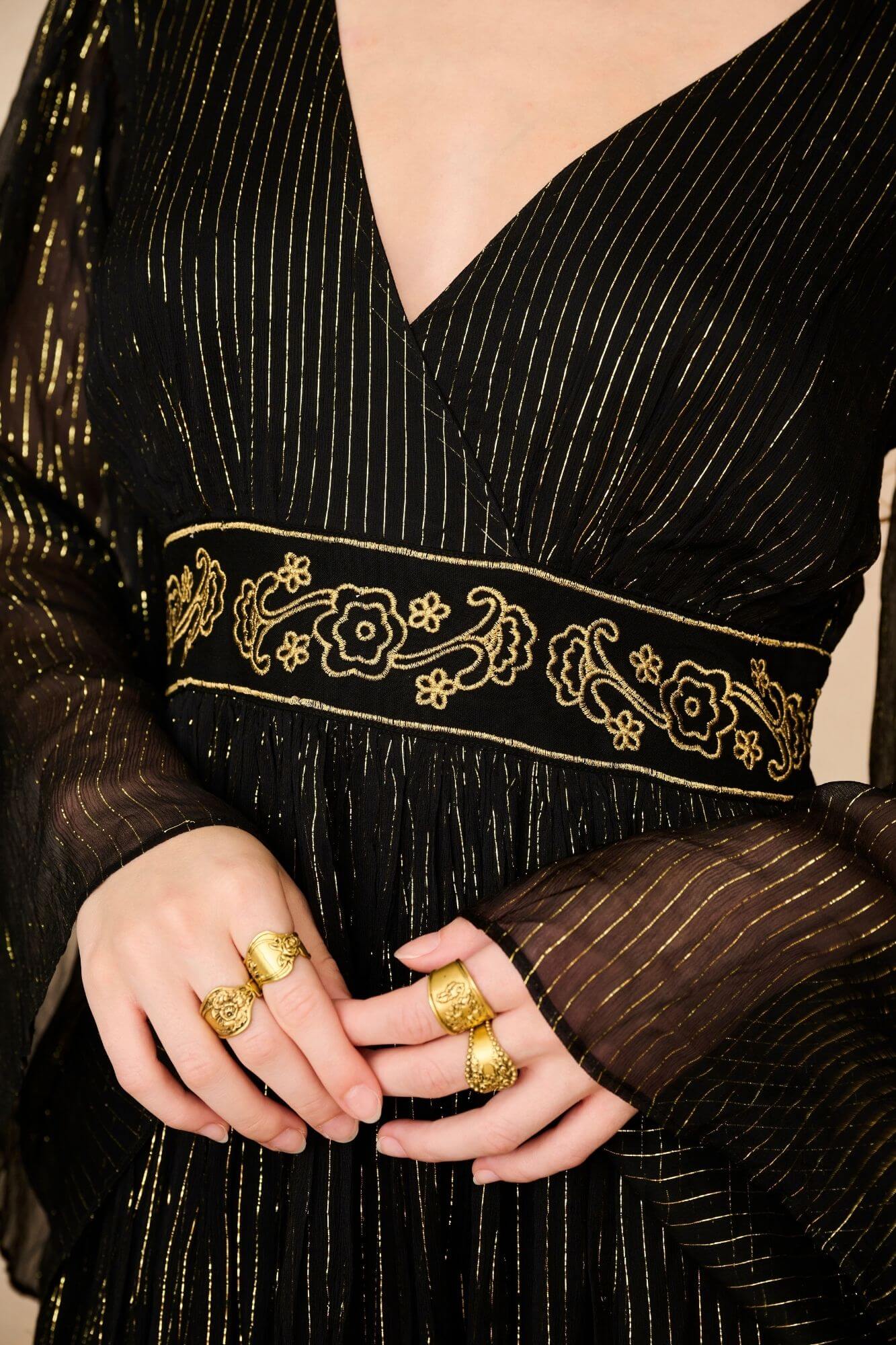 A model wearing a black maxi dress with sheer long flowy sleeves by the Hippie Shake, close up shot