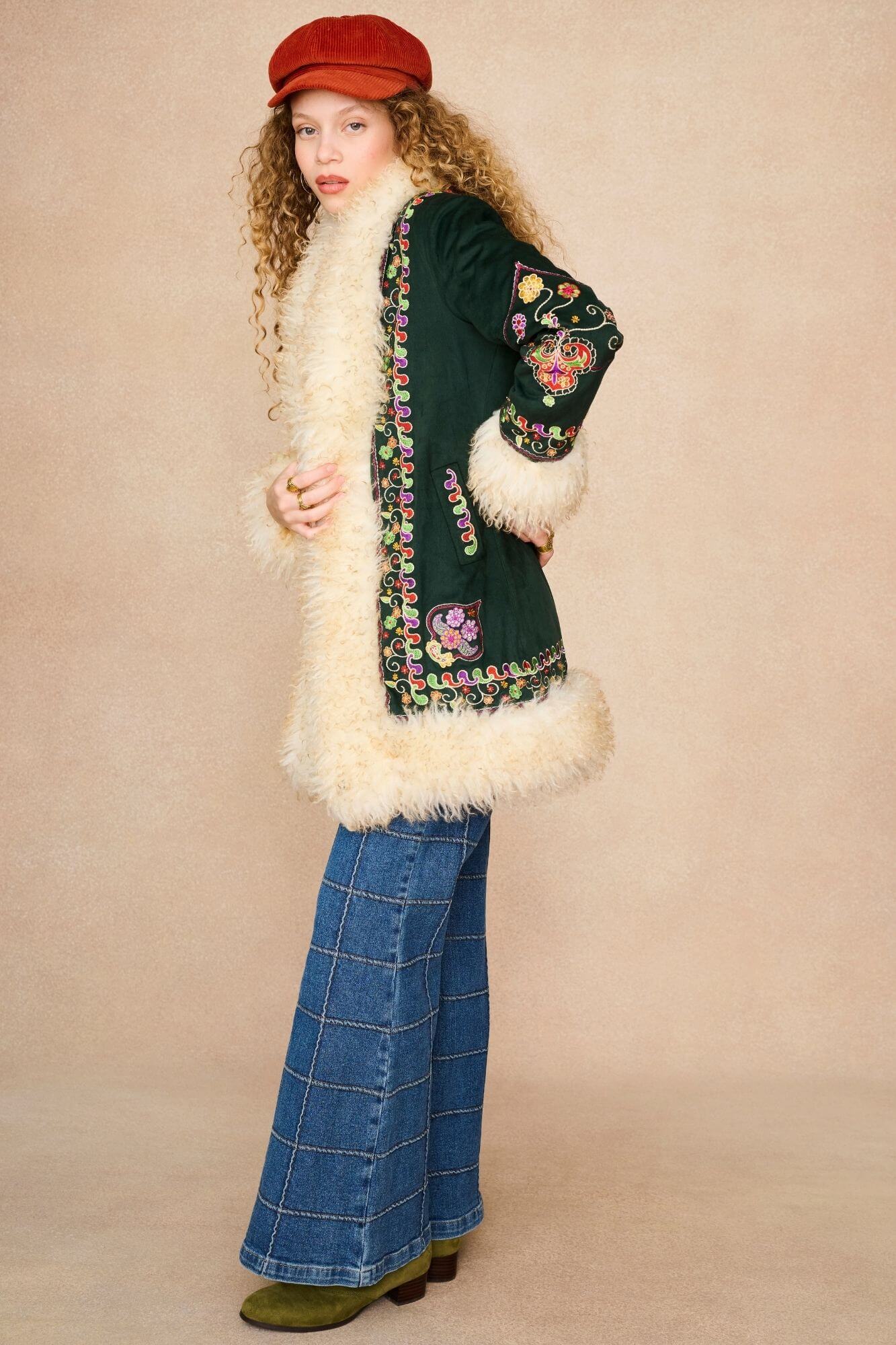 A model wearing a 70s dark green embroidered coat with a cream faux-fur collar and hem.