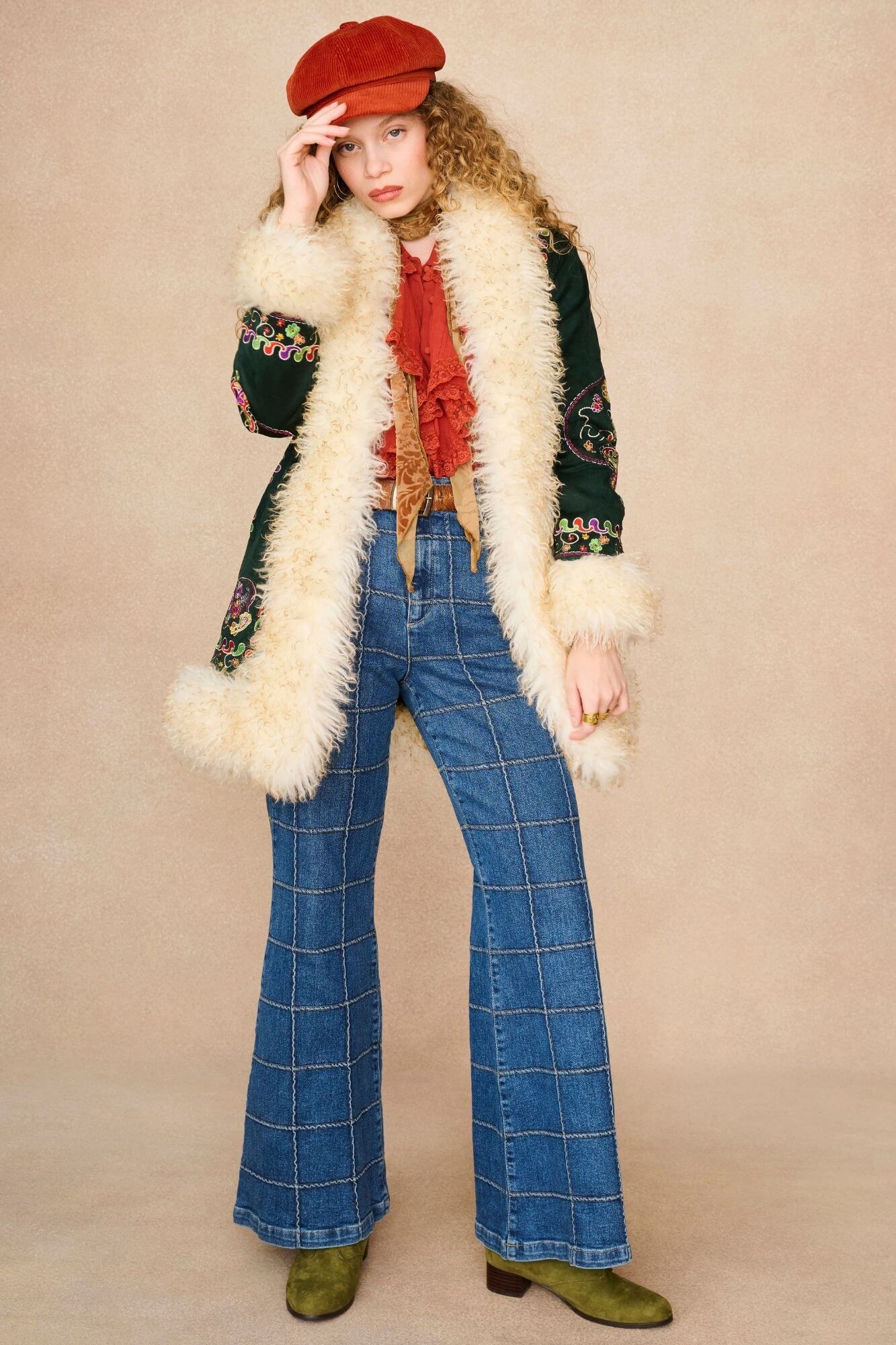 A model wearing a 1970s style outfit featuring a dark green embroidered jacket with a cream faux fur collar.