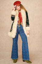 A model wearing a 1970s style outfit featuring a dark green embroidered jacket with a cream faux fur collar.