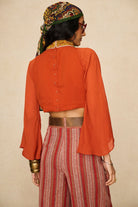 Model wearing 70s orange beaded top with striped trousers by The Hippie Shake, back view