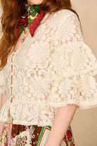 Person wearing a white lace top with a colorful scarf and patterned skirt.