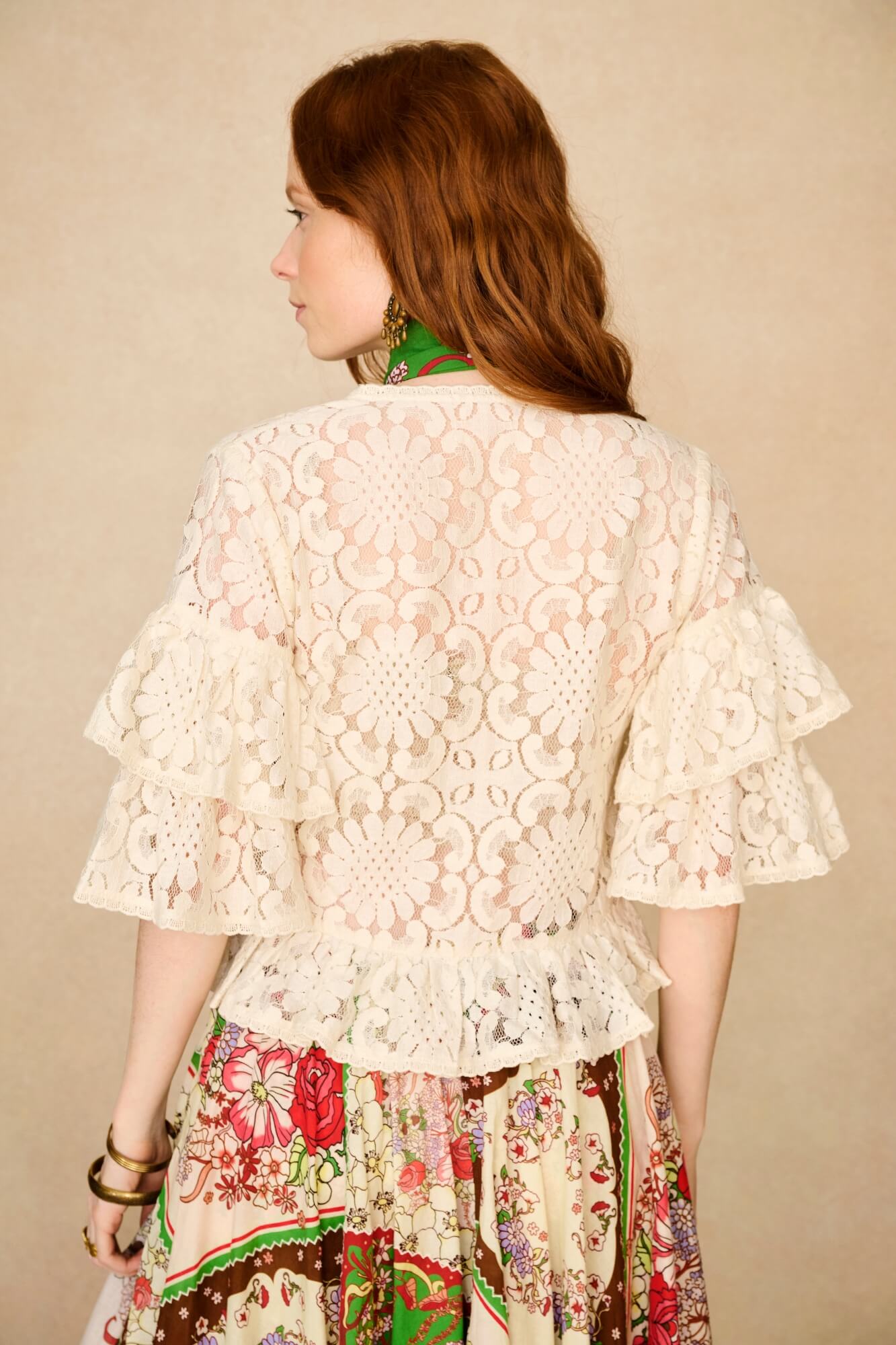 Woman wearing a lace top over a floral skirt against a beige background