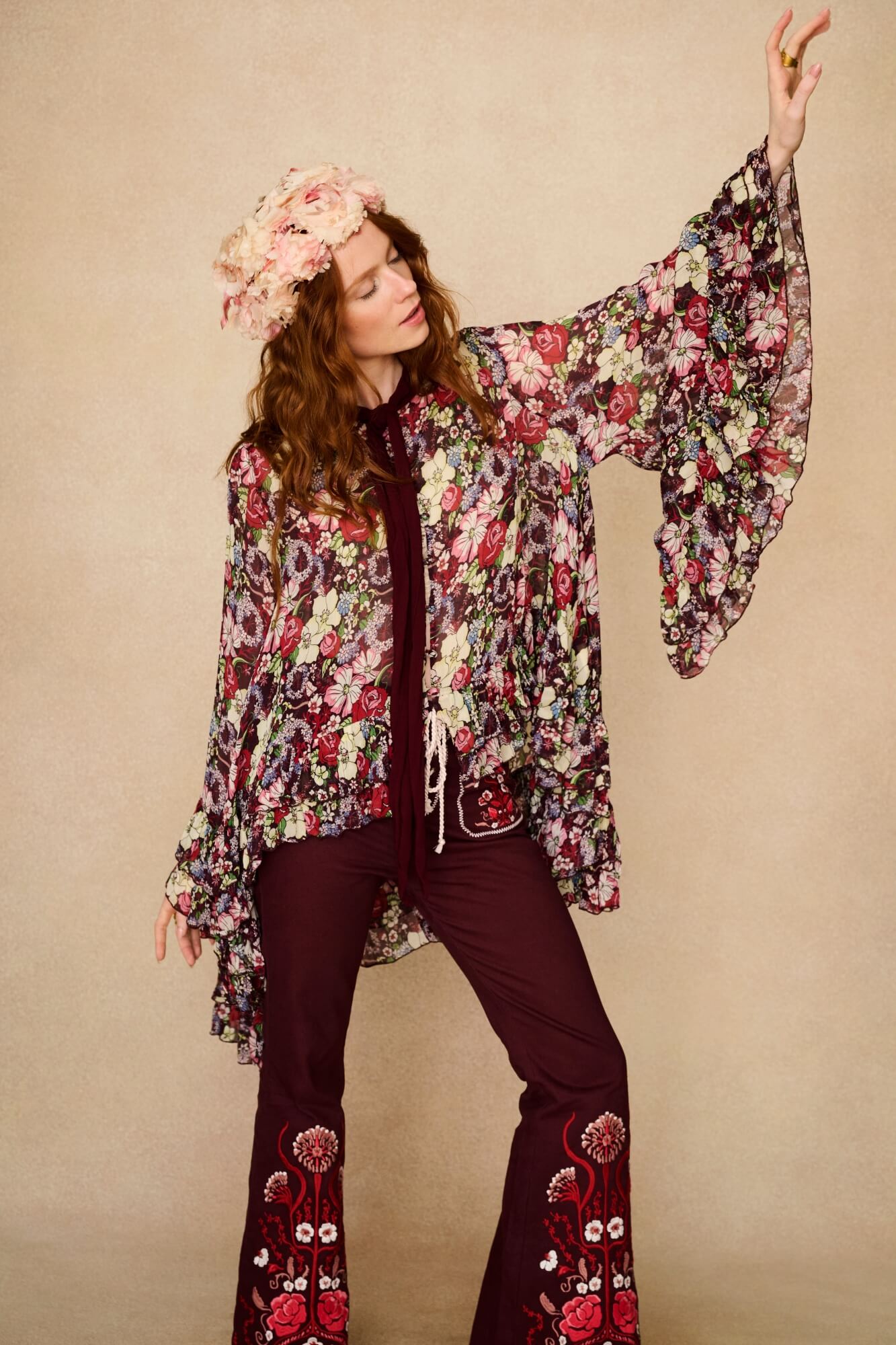 Woman wearing a floral cape top and pants against a beige background