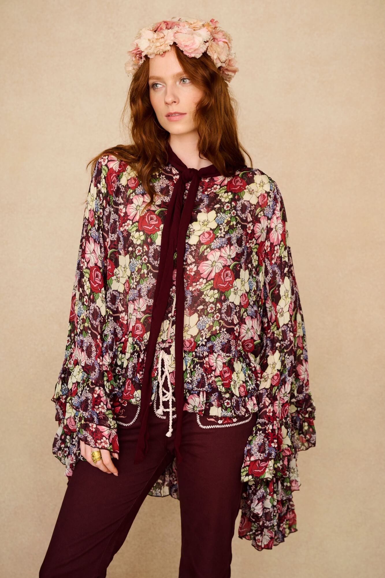 Woman wearing a floral cape top and headband against a beige background