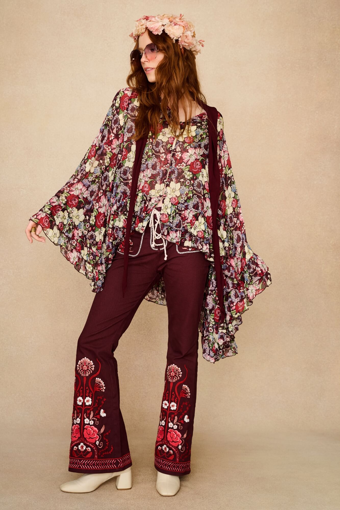 Woman wearing a floral cape top and embroidered pants on a beige background