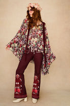 Woman wearing a floral cape top and embroidered pants on a beige background