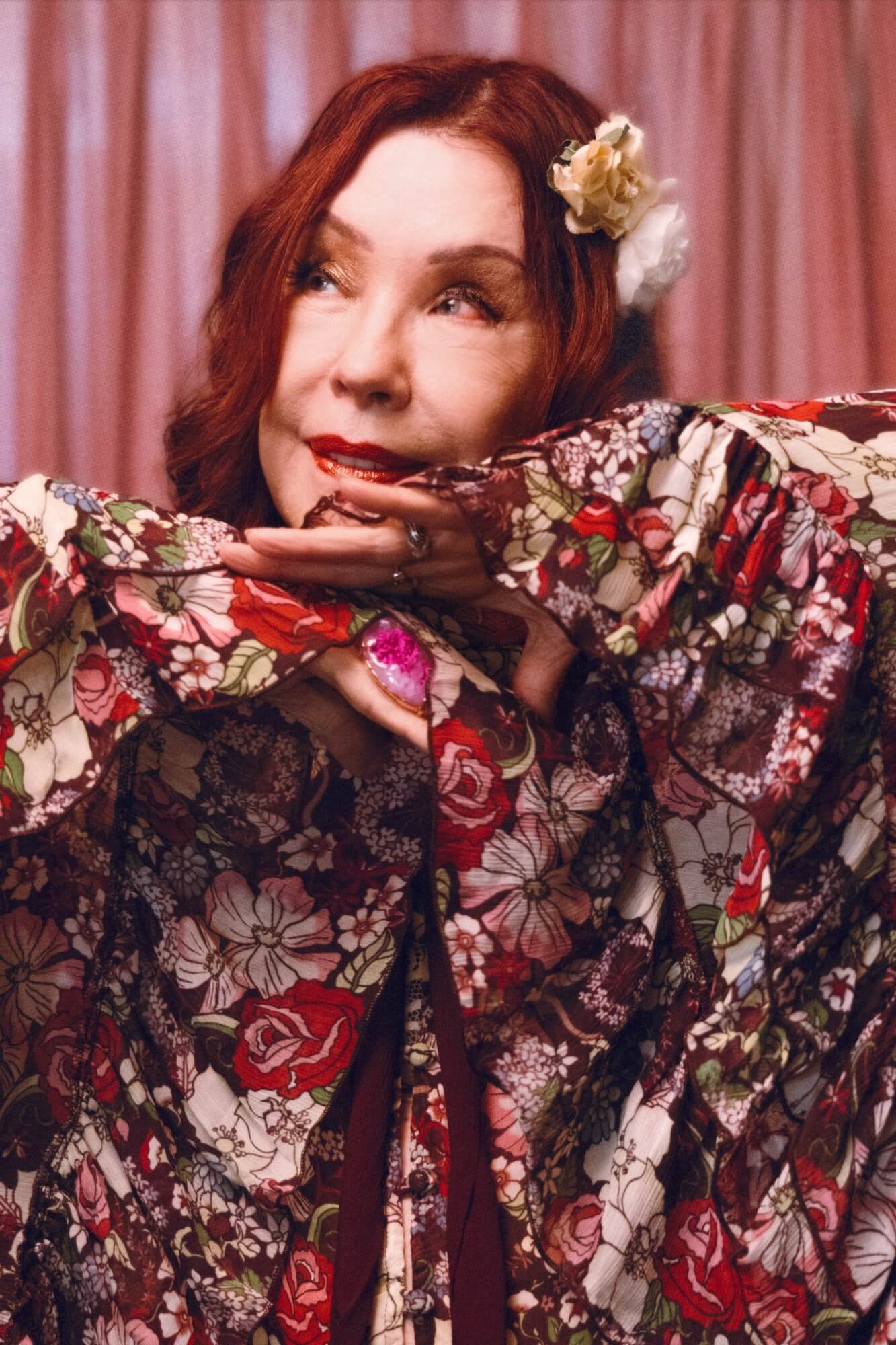 Person wearing a floral and patterned garment with a pink curtain background