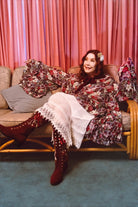 Woman in a floral top sitting on a couch with pink curtains in the background