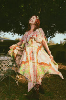 Woman in a patterned dress standing outdoors with trees in the background