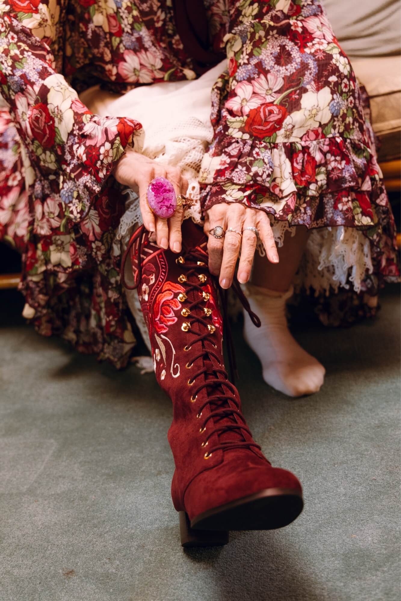 Person wearing a floral dress with red embroidered boot on a gray floor.