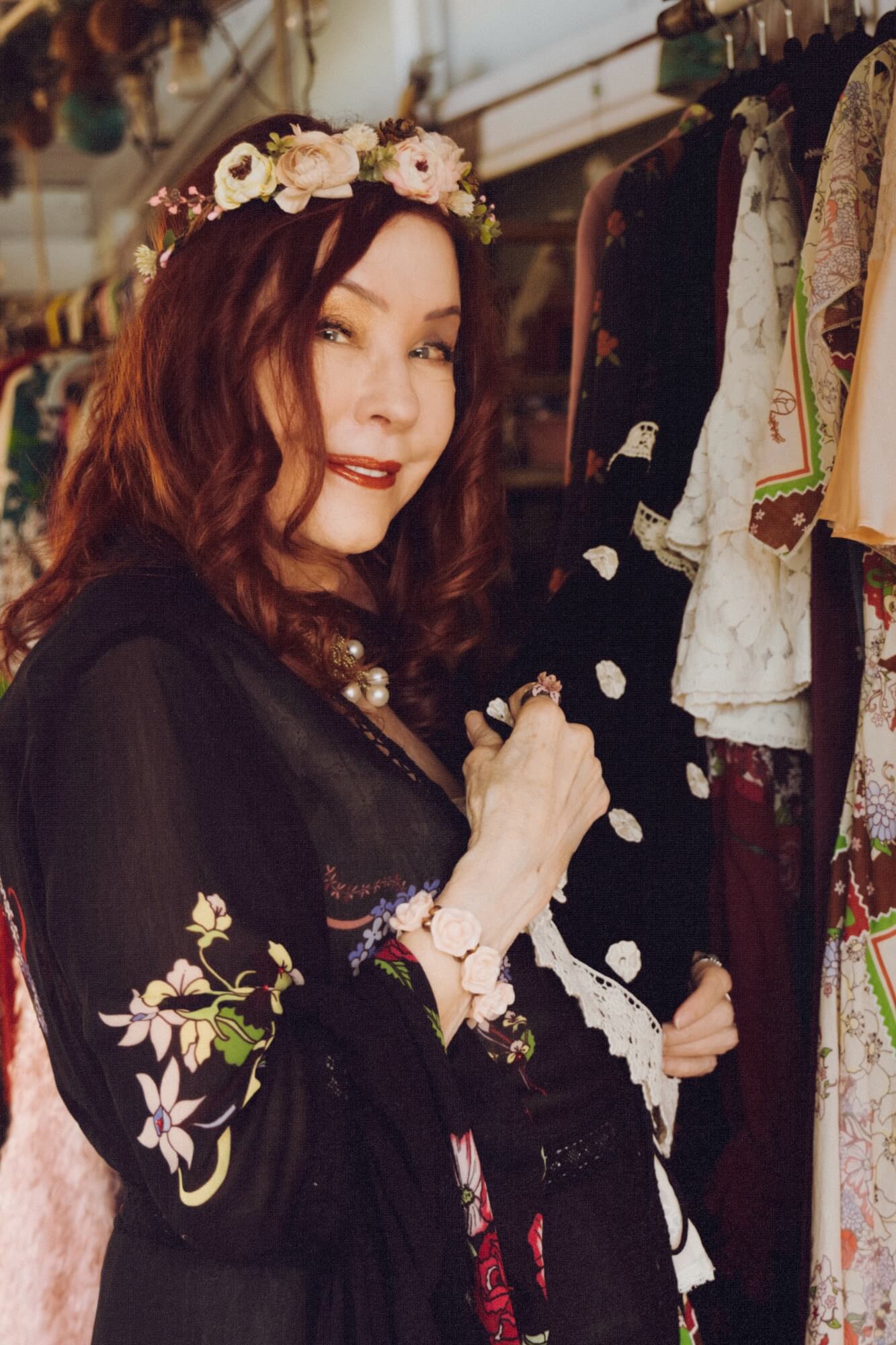 Woman wearing a black embroidered duster with floral accessories in a closet setting