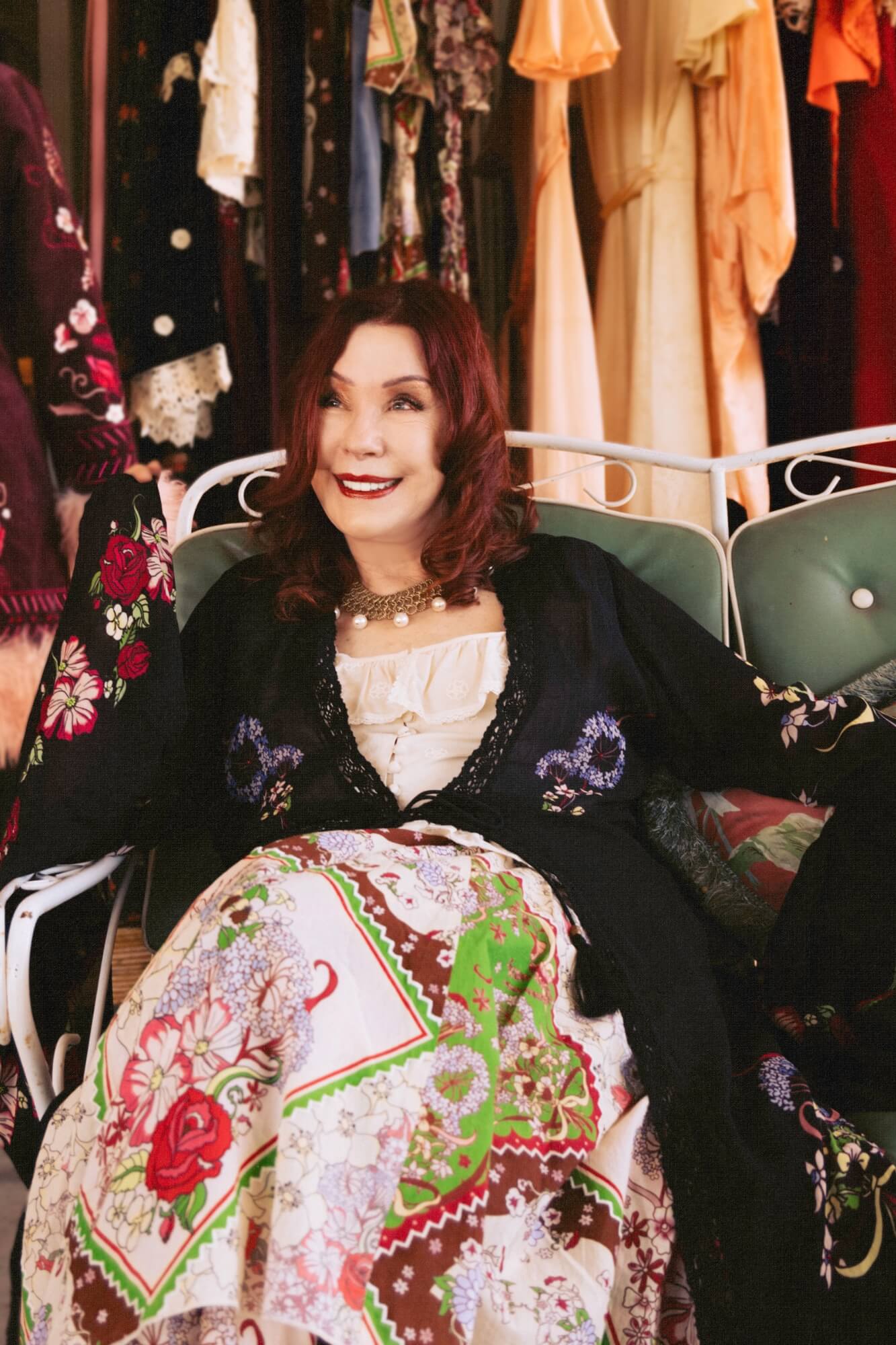 Woman sitting in a chair surrounded by colorful clothing and accessories