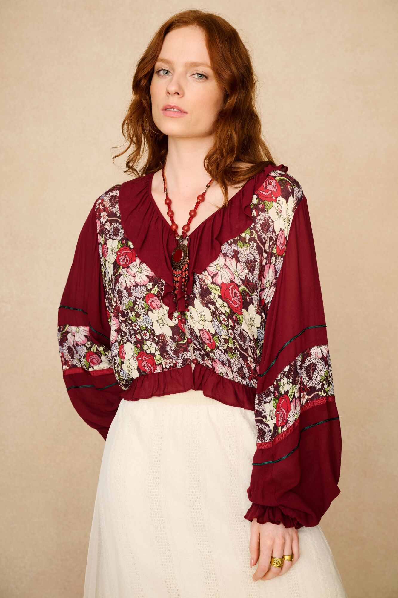Woman wearing a burgundy blouse with floral patterns against a beige background