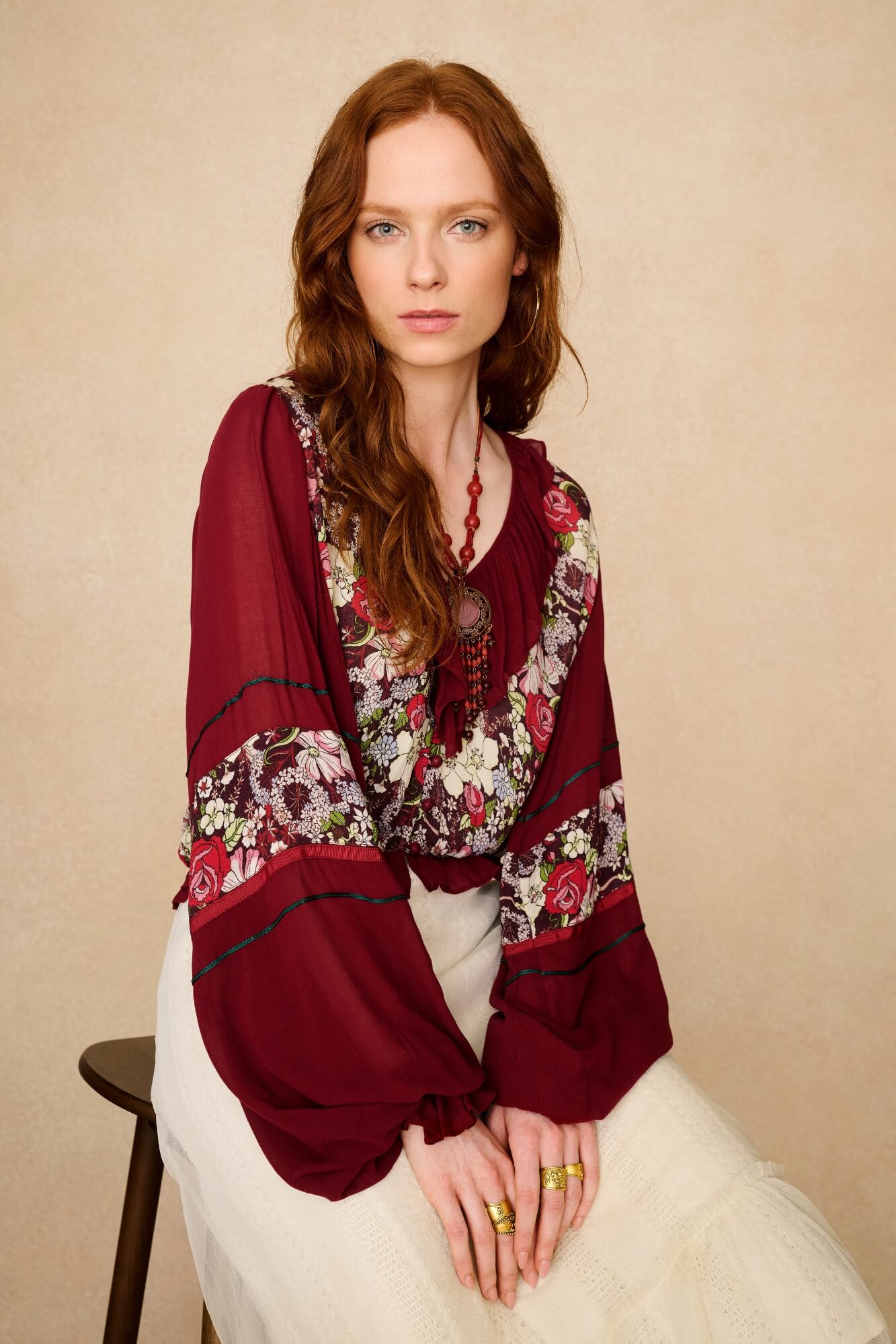 Woman wearing a burgundy floral blouse against a beige background