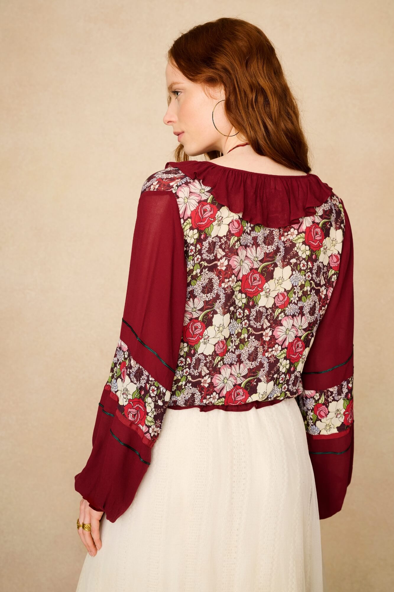 Woman wearing a floral blouse with burgundy accents against a beige background