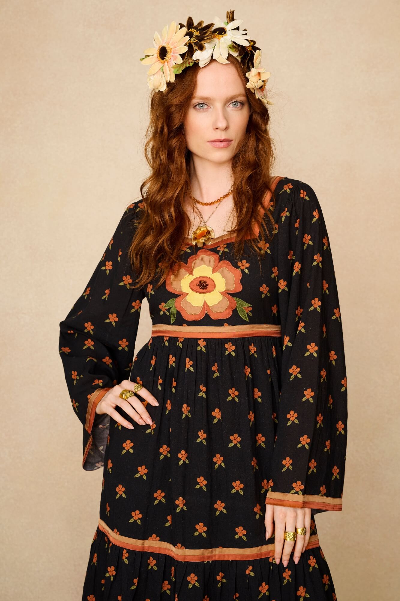 Woman wearing a black dress with floral patterns and a flower crown against a beige background