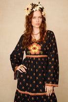 Woman wearing a black dress with floral patterns and a flower crown against a beige background