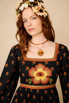 Woman wearing a black dress with floral patterns and a flower crown against a beige background